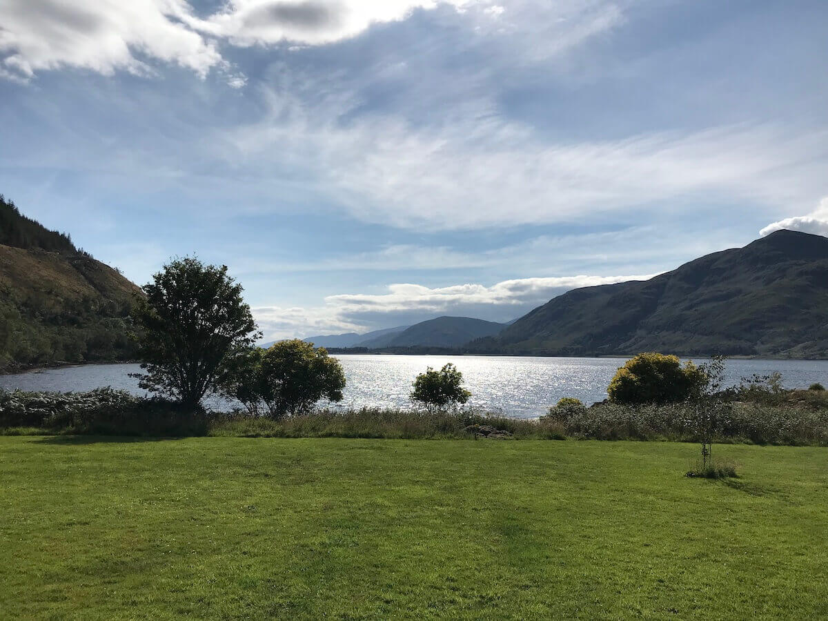 green lawn with loch and mountains behind