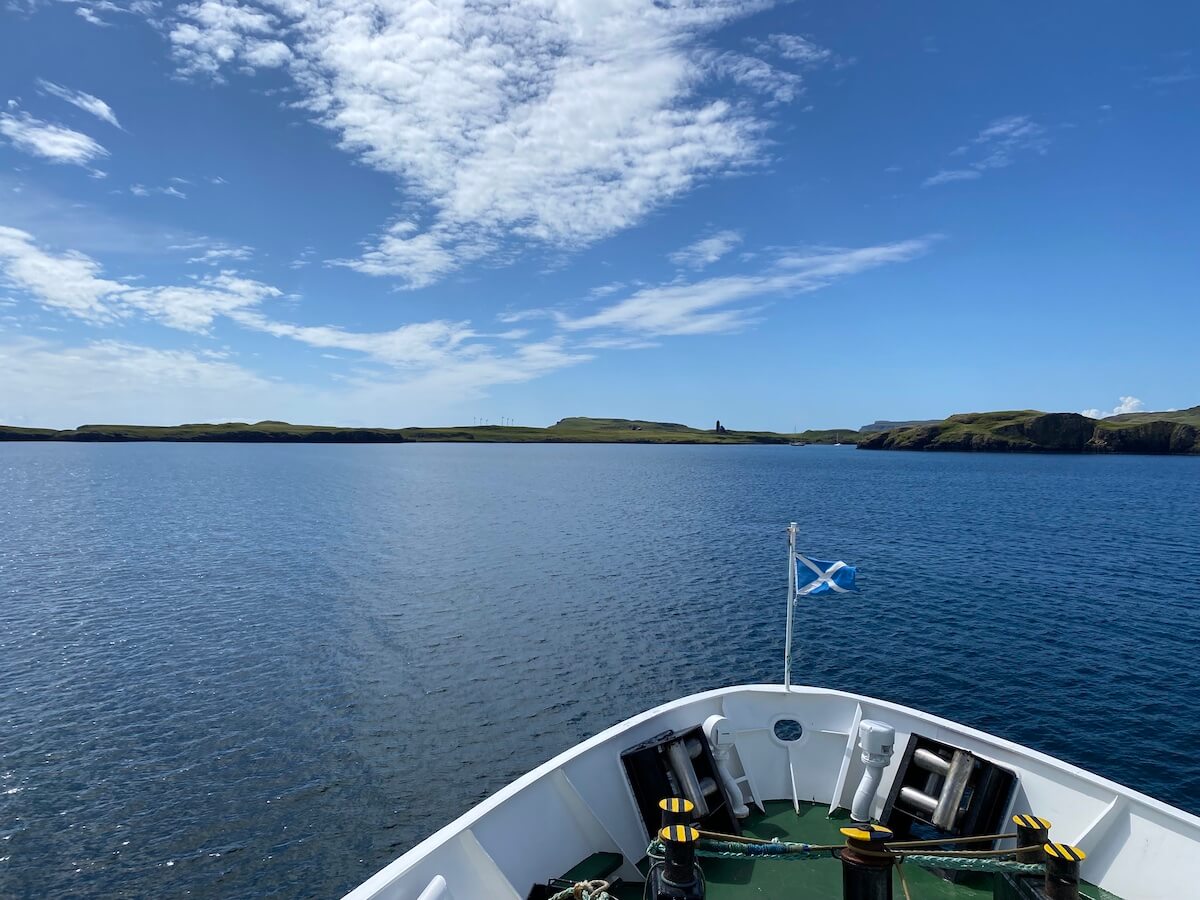 bow of ferry with a Scottish flag approaching a green island