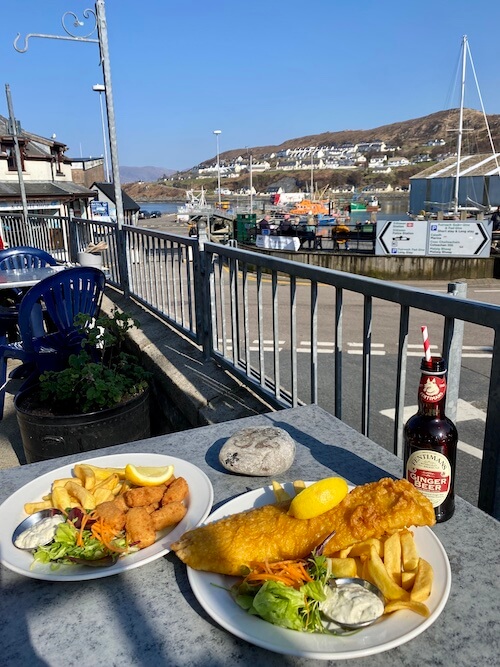 a terrace table with fish and chips with Mallaig harbour in the background