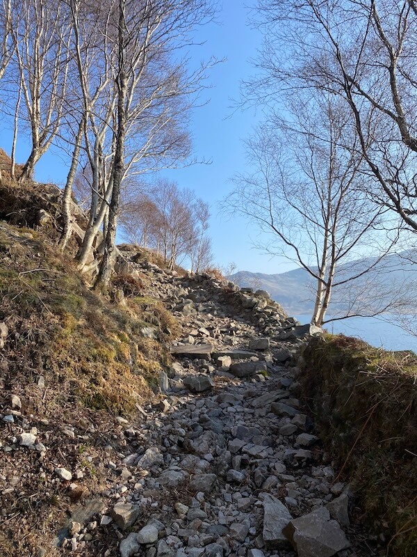 rocky path on hike along loch morar with bare trees and a blue sky