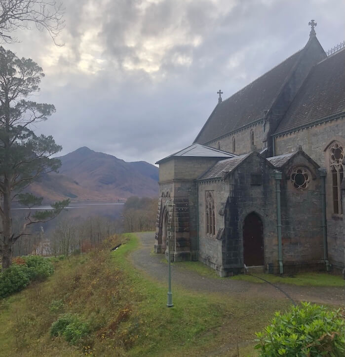 Stone church beside Loch Shiel with misty mountains and dark clouds in the background in the Scottish Highlands.